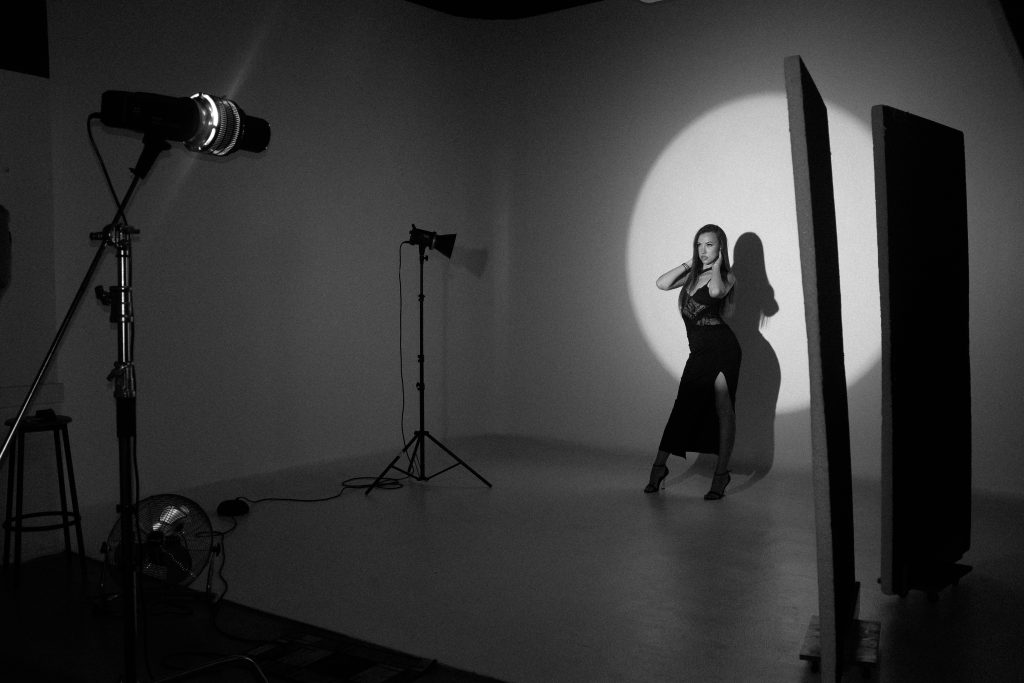 photography studio space with two tripods and two studio lights on them. there is a woman next to the tripods posing