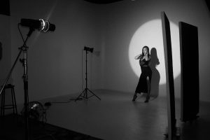 photography studio space with two tripods and two studio lights on them. there is a woman next to the tripods posing